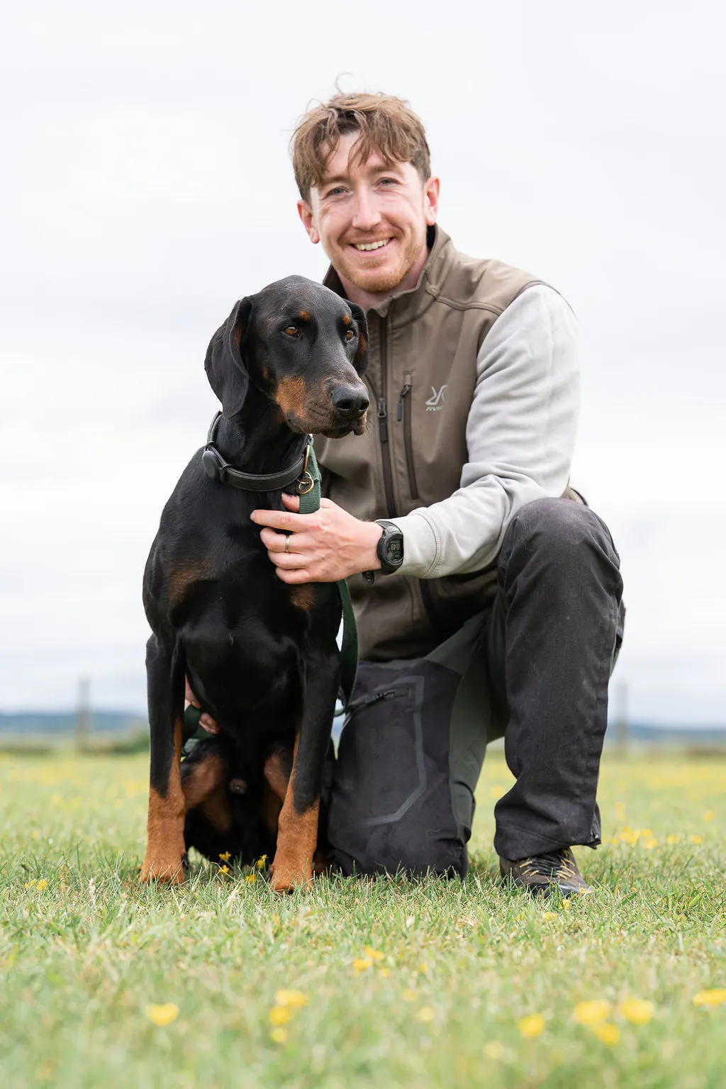 Kit Rowland kneeling outdoors with a Doberman